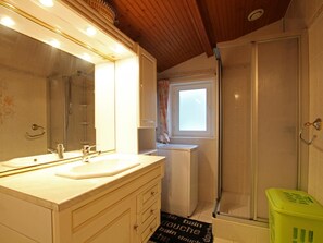 A bathroom with a double sink, a mirror, a shower, and a window.