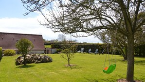 A well-maintained lawn with a swing set, a small tree, and a stone wall.