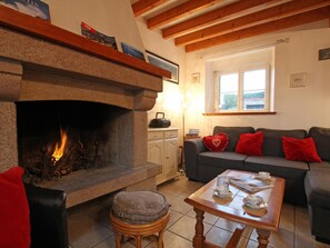 A cozy living room with a stone fireplace, a grey sofa with red cushions, a wooden coffee table, and a window with a view of the outside.