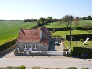 A stone house with a tiled roof, a driveway, and a fenced yard with a slide.