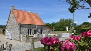 A stone building with a red-tiled roof, a signboard, and a white fence.
