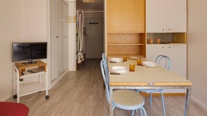 Un espace de vie compact comprenant un coin cuisine, une table à manger avec des chaises, un téléviseur posé sur un meuble et une petite chaise rouge.