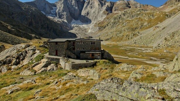 Un bâtiment en pierre doté d’un toit plat, situé dans une région montagneuse au terrain rocheux, surplombant une vallée.