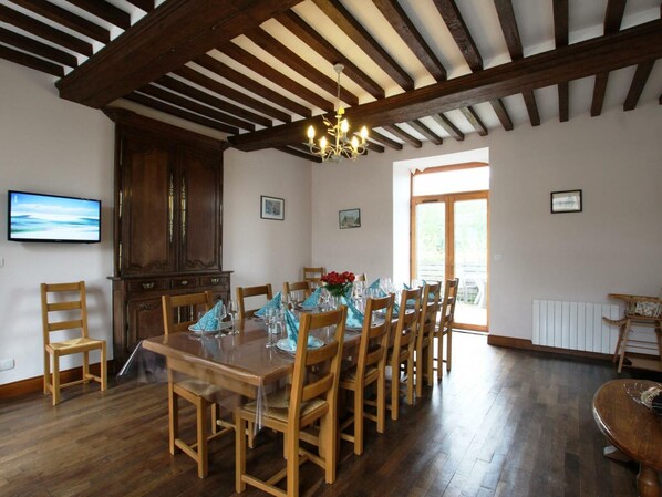 A dining area with a wooden table set for six, surrounded by wooden chairs. A chandelier hangs from the ceiling, and there is a wooden cabinet to the left.