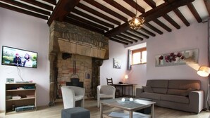 A cozy living room with a stone fireplace, a television, a sofa, and a coffee table. - Charming family cottage, 12 beds, garden and terrace (La Ronde-Haye)