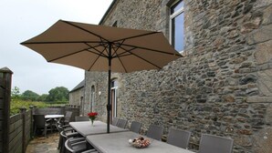An outdoor dining area with a stone building, a table with chairs, and a large umbrella. - Charming family cottage, 12 beds, garden and terrace (La Ronde-Haye)