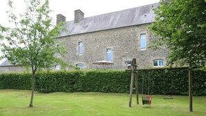 A stone building with a grassy yard, a swing set, and a hedge. - Charming family cottage, 12 beds, garden and terrace (La Ronde-Haye)