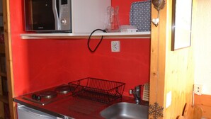 Une cuisine compacte avec un mur rouge, un four à micro-ondes, une bouilloire et un évier.