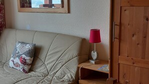 Une chambre avec un canapé beige, une lampe rouge, une armoire en bois et une fenêtre donnant sur des arbres.