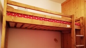 Un lit superposé avec un matelas à motifs rouges et une échelle en bois.