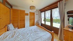 A bedroom with a large bed, wooden wardrobe, a television on a wooden cabinet, and a window with curtains. - 3-room apartment with garage, 6 sleeps in Grand-Bornand (Le Grand-Bornand)