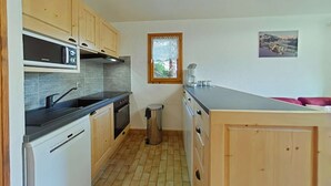 A compact kitchen with wooden cabinets, a built-in microwave, a stainless steel range hood, a window with a view, and a small trash bin. - 3-room apartment with garage, 6 sleeps in Grand-Bornand (Le Grand-Bornand)