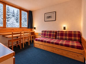 A cozy cabin interior with a wooden desk, chairs, a plaid sofa, and a window with a snowy view. - Cozy studio Arc 1800, 2 people, Wifi, pets allowed (Les Arcs 1800)