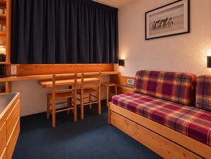 A cozy room with a wooden desk, two chairs, a plaid sofa, and a framed picture on the wall.