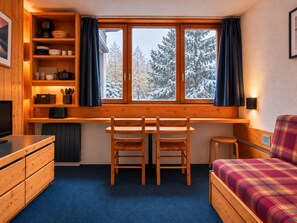 Um quarto acolhedor com escrivaninha de madeira, duas cadeiras, cama com roupa de cama xadrez e janela com cortinas.