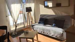 A living room with a sofa, a small table, a floor lamp, and a TV on a stand.