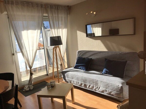 Un salon avec un canapé, une petite table, une lampe sur pied et un téléviseur posé sur un meuble.