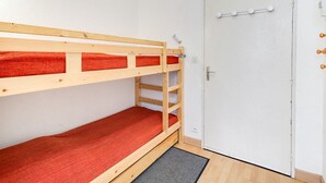 A bunk bed with red bedding in a room with white walls and a door with a handle and a lock.