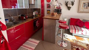 A compact kitchen with red cabinets, a small island, and a dining area with a red and white patterned tablecloth. - D104 - 42 m2 - 2P+cab - 4/6 pers (Prapoutel)