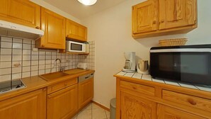 Una cocina con armarios de madera, microondas, cafetera y un cubo de basura.