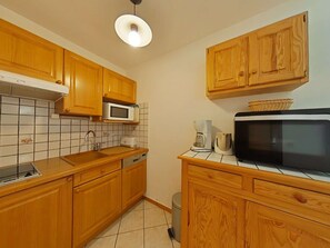 A kitchen with wooden cabinets, a microwave, a coffee maker, and a trash bin.