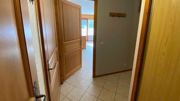 Un pasillo con puertas de madera y suelo de baldosas que conduce a un espacio abierto con vista a zonas verdes.