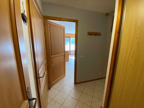 A hallway with wooden doors and a tiled floor leading to an open space with a view of greenery outside. - Cozy apartment in Grand Bornand - 6 people, balcony, parking, near center (Le Grand-Bornand)