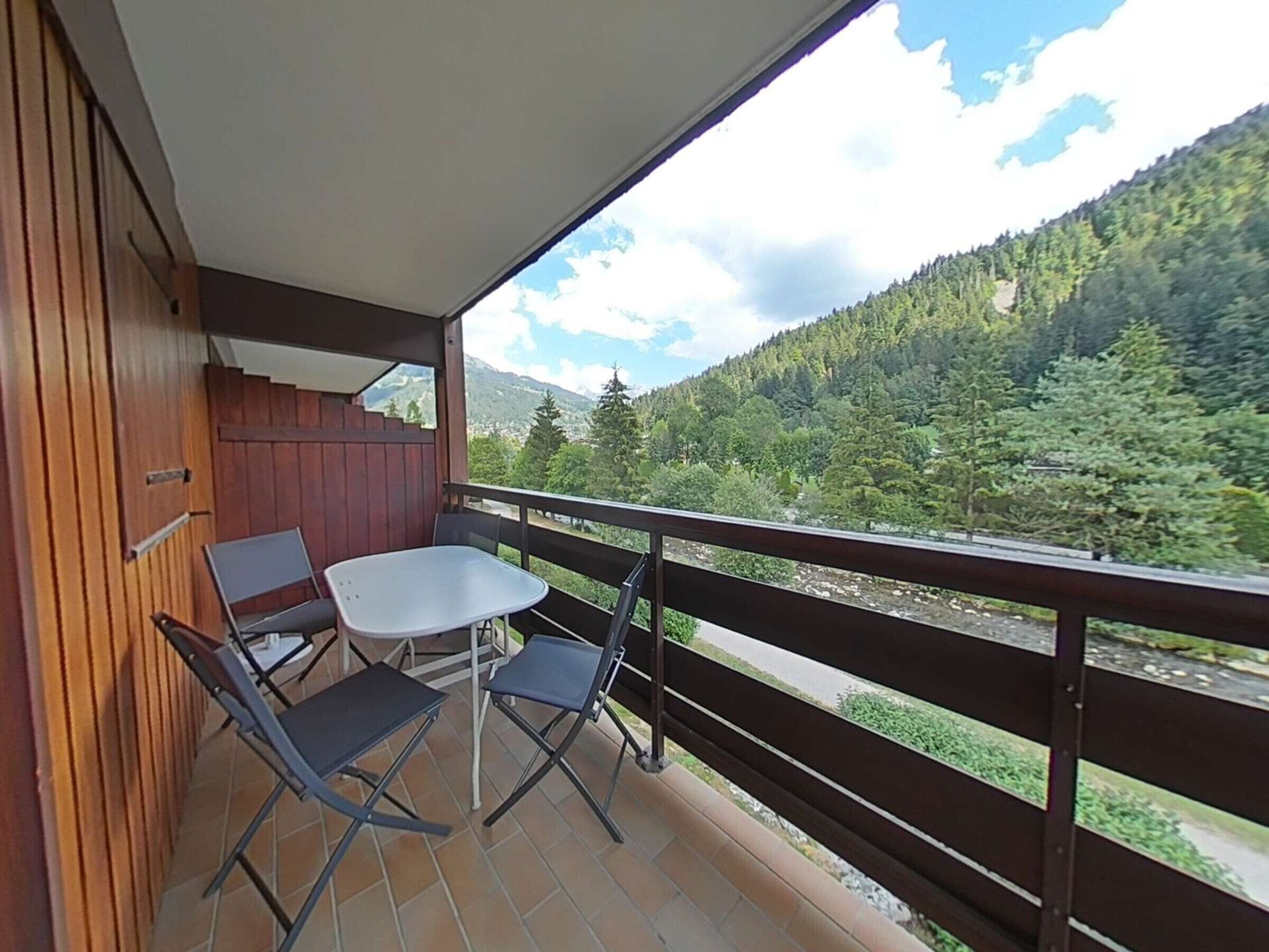 A balcony with a table and chairs, wooden paneling, and a view of a forested mountain.