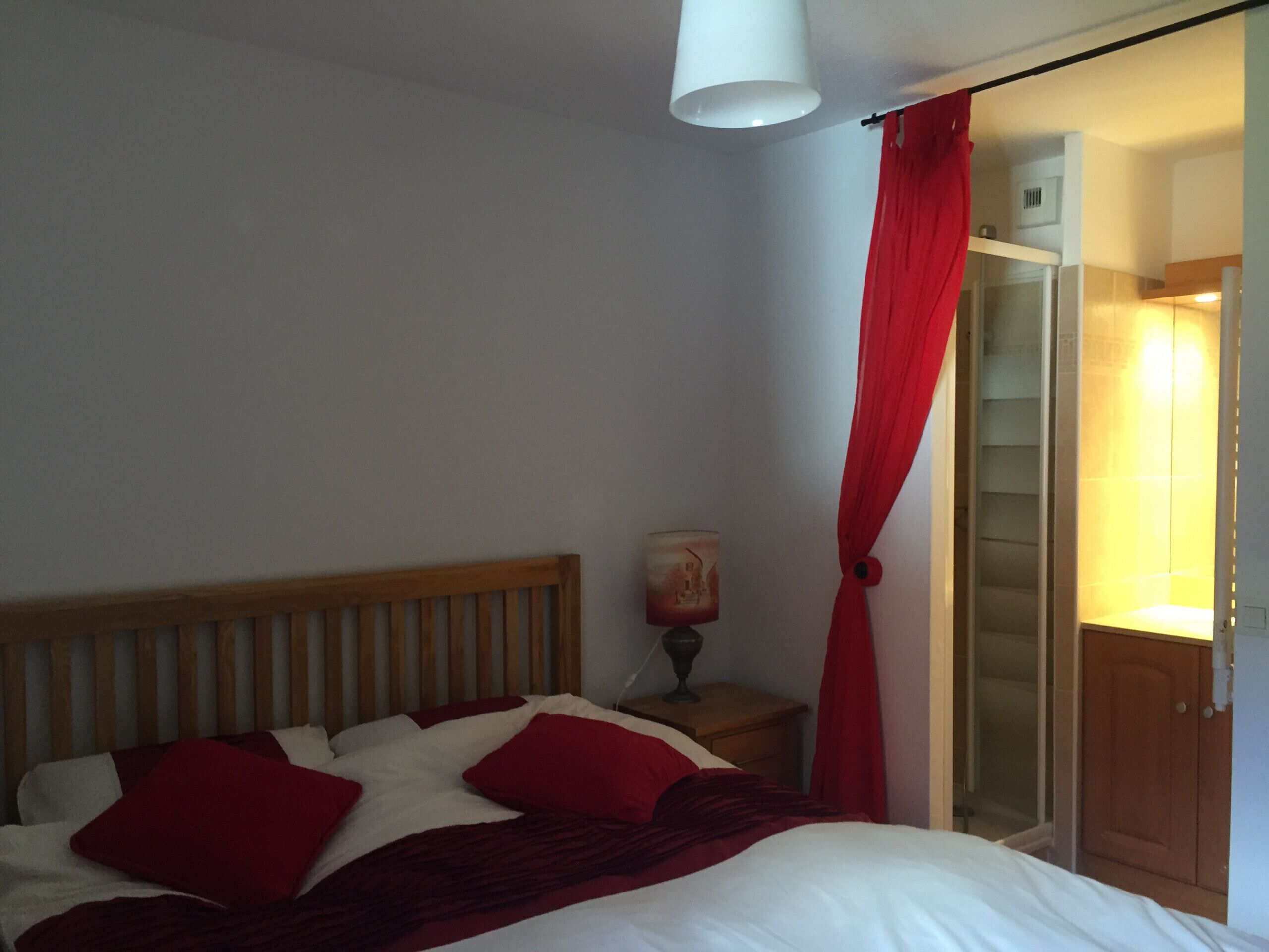 A bedroom with a bed, a nightstand, a lamp, and a red curtain.