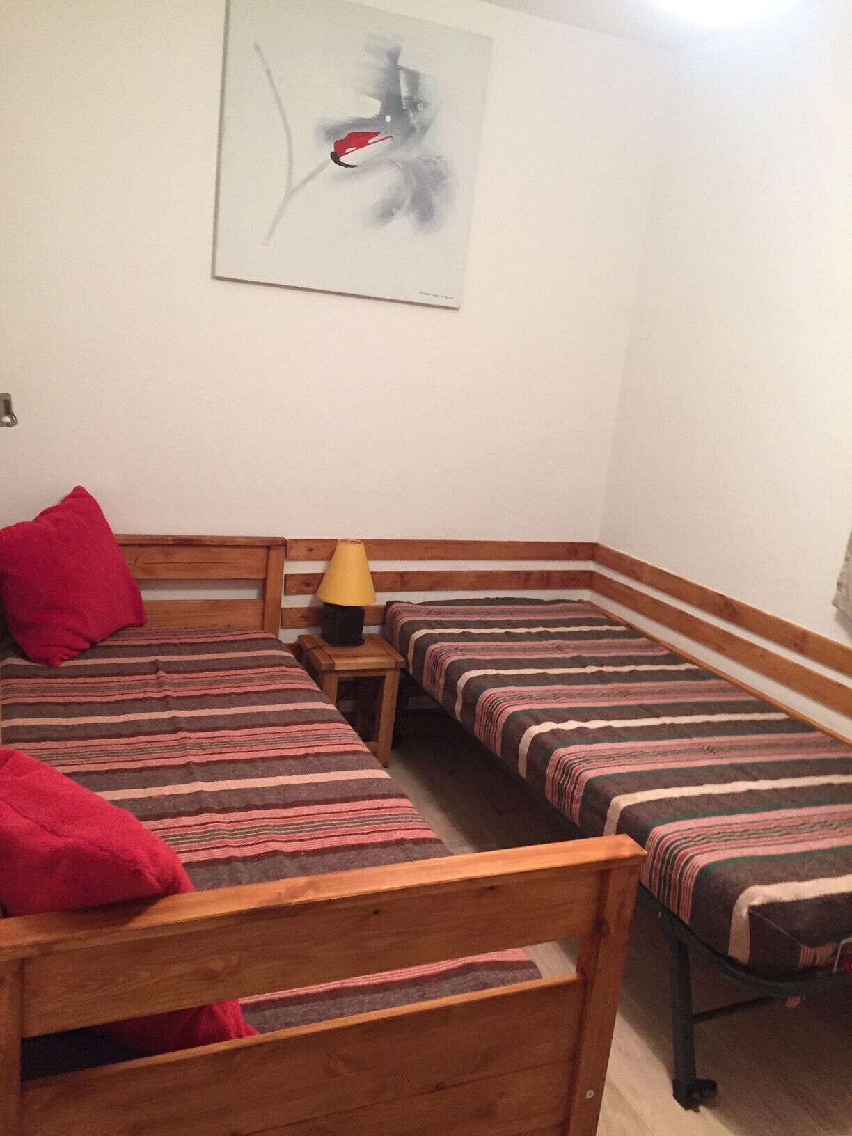 A room with two single beds, a wooden headboard, a small table with a lamp, and a painting on the wall.