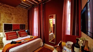 A bedroom with a stone wall, a bed with red bedding, a mirror, a TV, and a breakfast setup with a bottle of wine and a glass of orange juice. - D1GG Colorado (Paris)