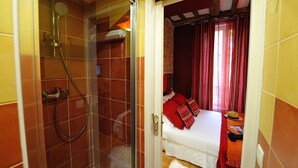 A bathroom with a glass-enclosed shower and a visible bed with red curtains and pillows. - D1GG Colorado (Paris)