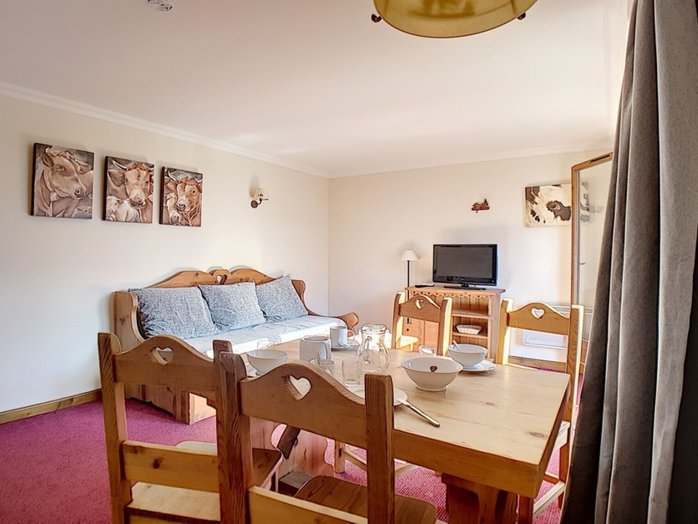 A cozy room with a wooden bed, a dining table with chairs, a television, and artwork on the walls.