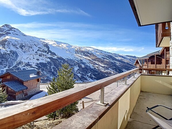 A mountain view from a balcony with wooden railings, a small building, and a clear sky.