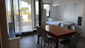 A small, modern room with a wooden table, four chairs, a bed, a TV, and a window with curtains. - Charming T2 Cabin with terrace and pool in Port Barcarès (Port Barcarès)