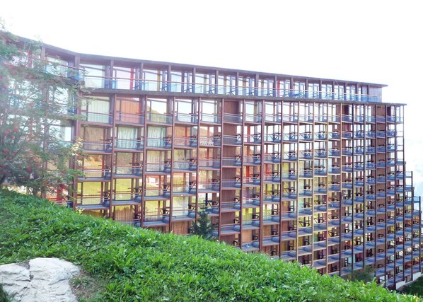 Stunning hotel building with a grid-like facade and lush green surroundings, featuring large windows and balconies with railings.