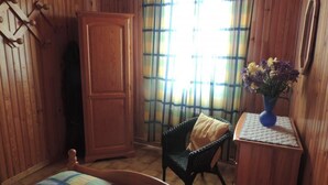 A wooden-paneled room with a bed, a chair, a cabinet, and a window with curtains.