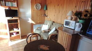 A cozy room with a round table, chairs, a television, a bookshelf, a microwave, and a clock on the wall.