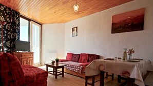 Ein gemütliches Wohnzimmer mit einem roten Sofa, einem Holztisch und einem für zwei Personen gedeckten Esstisch.