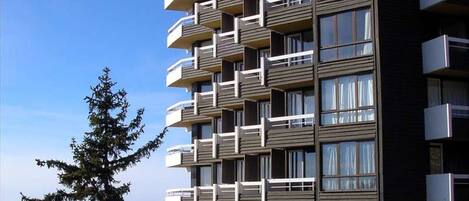 A multi-story residential building with balconies, large windows, and a clear sky.