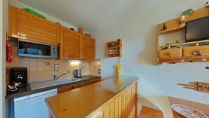 Une cuisine compacte dotée de meubles en bois, d’un four à micro-ondes, d’une bouilloire et d’un petit réfrigérateur.