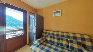 Une pièce avec un canapé à carreaux, un réfrigérateur, une fenêtre donnant sur une montagne et un tableau encadré accroché au mur.