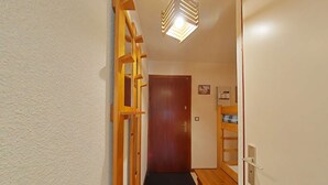 Un couloir étroit avec une échelle en bois, une porte, un petit banc et un luminaire au plafond.
