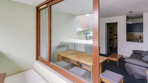 Une pièce dotée d’une grande fenêtre, d’une table en bois avec des bancs, d’un canapé et d’un coin cuisine.