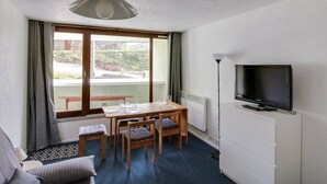 Une pièce comprenant une table à manger, des chaises, un téléviseur et donnant sur l’extérieur.