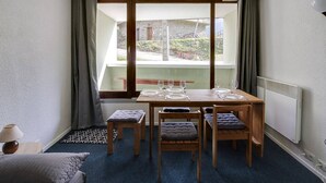Un petit coin repas avec une table dressée pour quatre personnes, des chaises en bois avec des coussins, une vue sur un bâtiment en pierre à l’extérieur et un radiateur au mur.