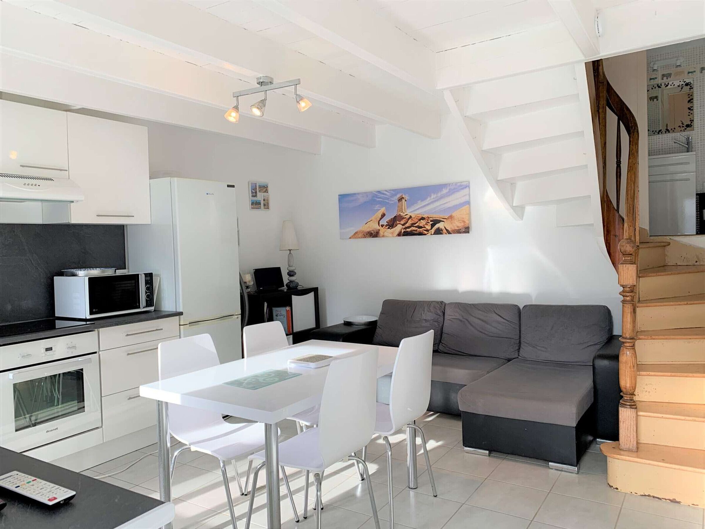 A modern kitchen with white cabinets, a dining area with a white table and chairs, and a gray sofa.