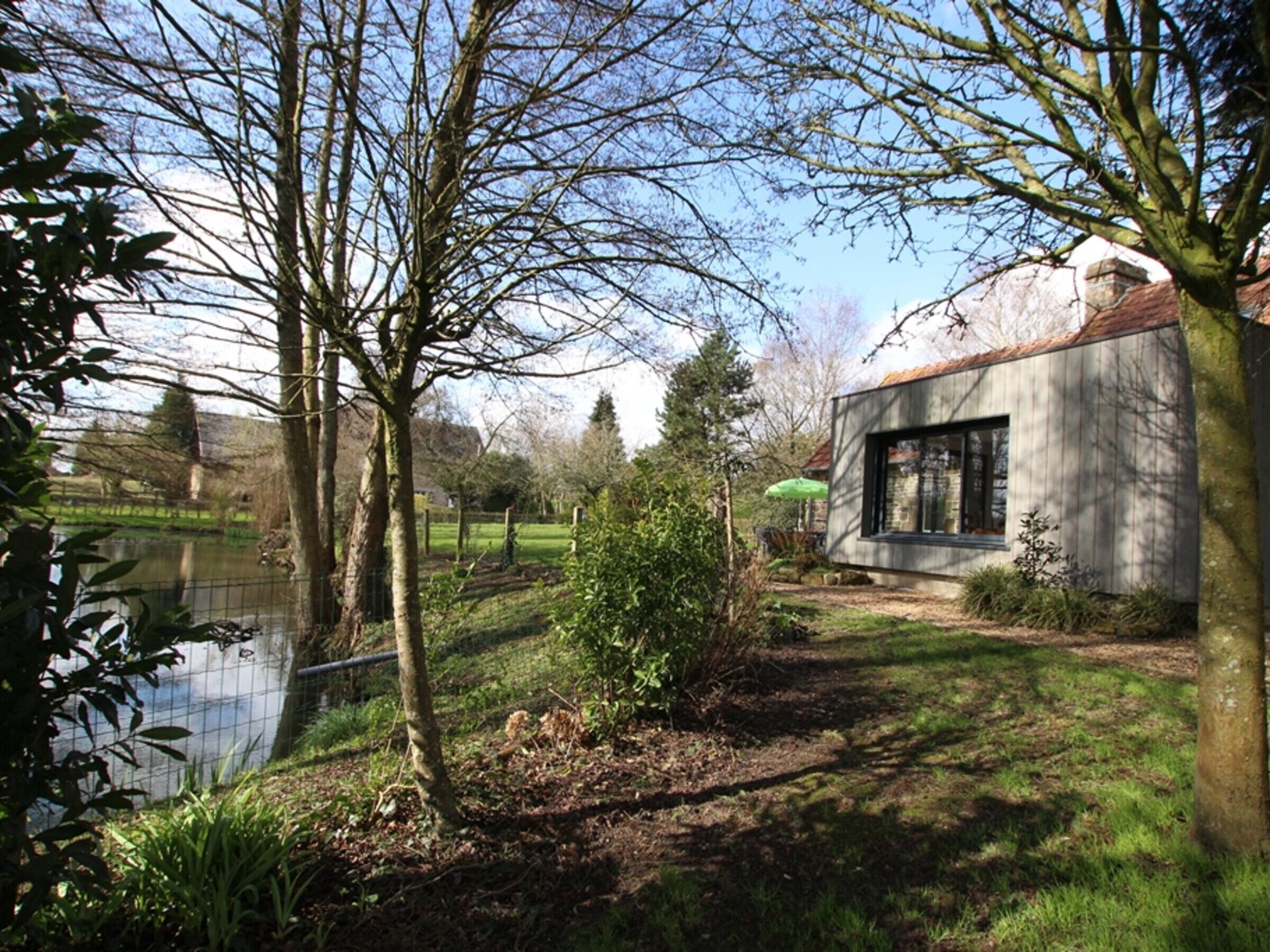 A modern house with a large window, surrounded by a garden and a body of water.