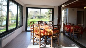 A dining area with a table set for six, large windows, and a view of a garden and lake.