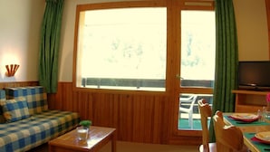 Una sala de estar acogedora con un sofá a cuadros, una mesa de centro de madera y un comedor con sillas y una mesa.